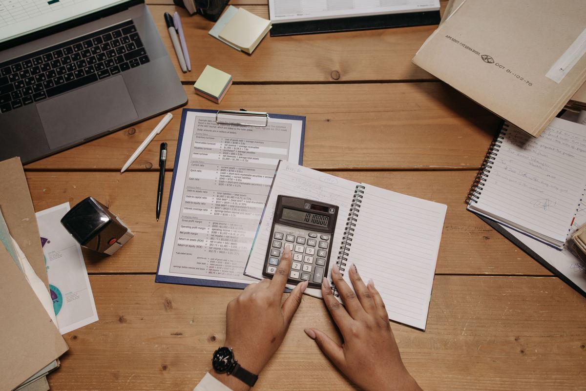 Hands using a calculator next to a notebook and budget worksheet